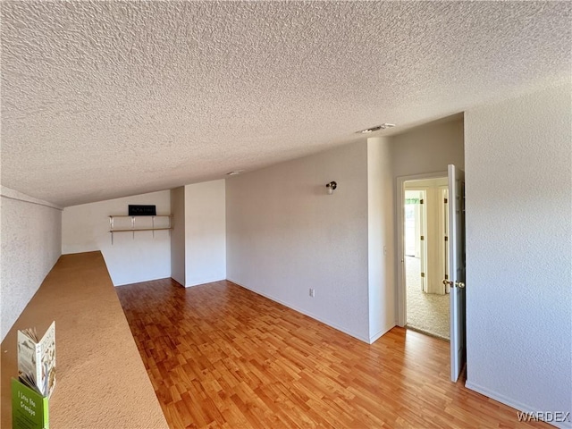 interior space featuring a textured ceiling, a textured wall, wood finished floors, and visible vents