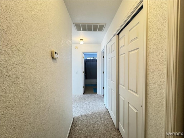 hall with a textured wall, carpet flooring, visible vents, and baseboards