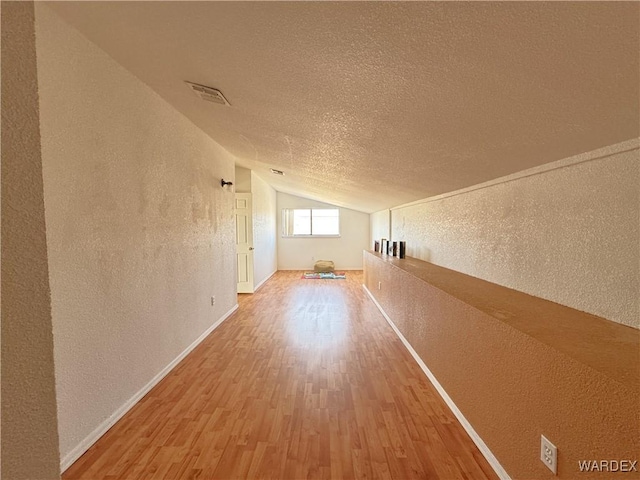 bonus room with visible vents, a textured wall, wood finished floors, vaulted ceiling, and a textured ceiling