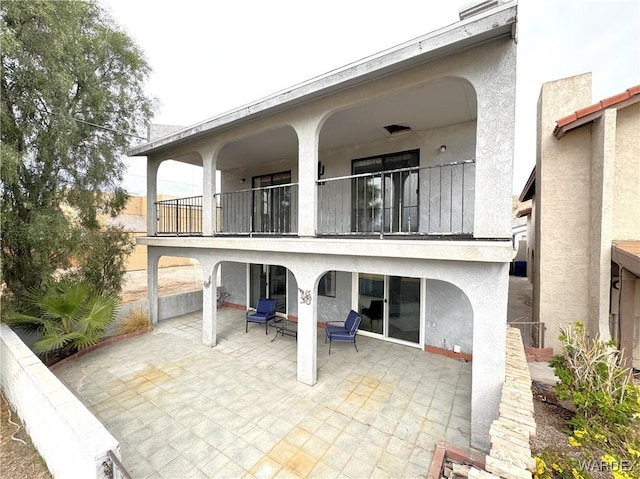 back of house with a balcony, stucco siding, and a patio