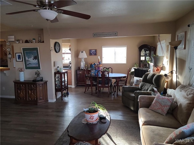 living area with a ceiling fan, baseboards, and dark wood-type flooring