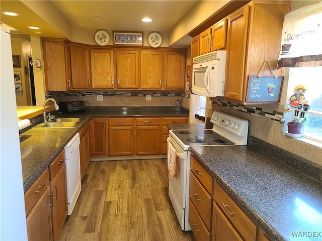 kitchen featuring white appliances, dark countertops, light wood-style flooring, brown cabinets, and a sink