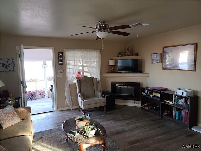 living area featuring a wealth of natural light, dark wood-type flooring, a glass covered fireplace, and visible vents