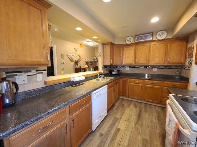 kitchen with light wood-style flooring, a peninsula, white appliances, a sink, and dark countertops