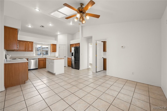 kitchen with lofted ceiling with skylight, brown cabinets, stainless steel appliances, light countertops, and light tile patterned flooring