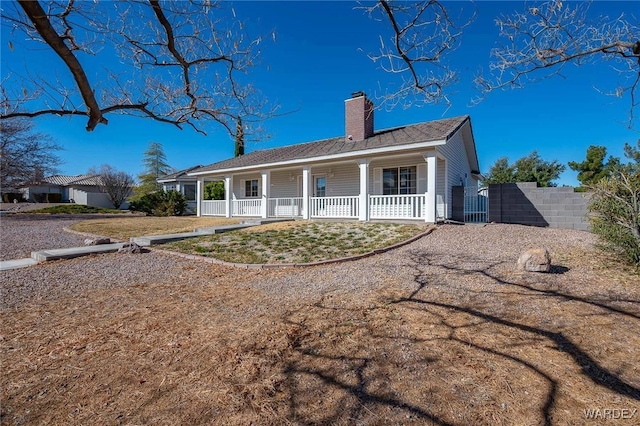 view of front of house featuring covered porch, fence, and a chimney