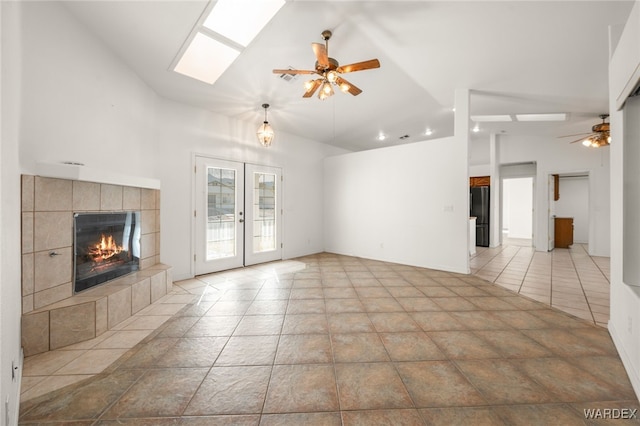 unfurnished living room featuring lofted ceiling with skylight, ceiling fan, a fireplace, and french doors