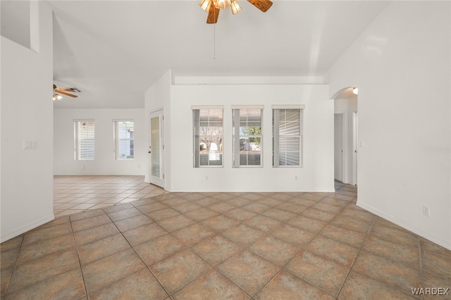 unfurnished living room with arched walkways, vaulted ceiling, a ceiling fan, and tile patterned floors