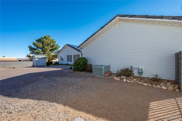 view of side of home featuring an outbuilding, central AC, fence, driveway, and a storage unit