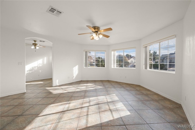 tiled empty room with baseboards, visible vents, arched walkways, and a ceiling fan