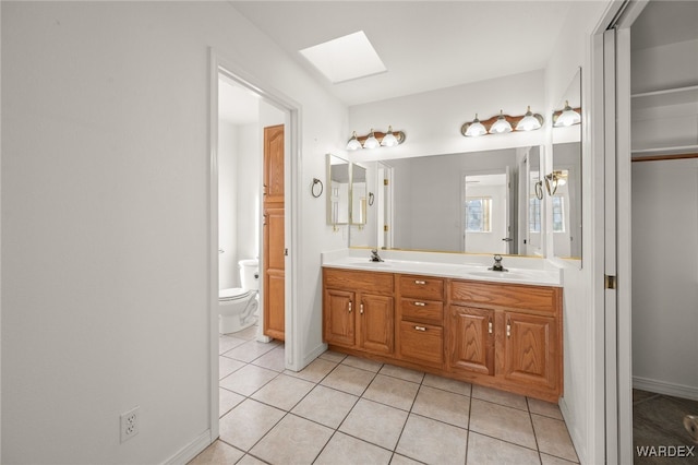 bathroom featuring a skylight, double vanity, toilet, a sink, and tile patterned flooring