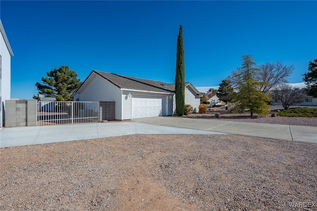 view of property exterior with concrete driveway, fence, an attached garage, and a gate