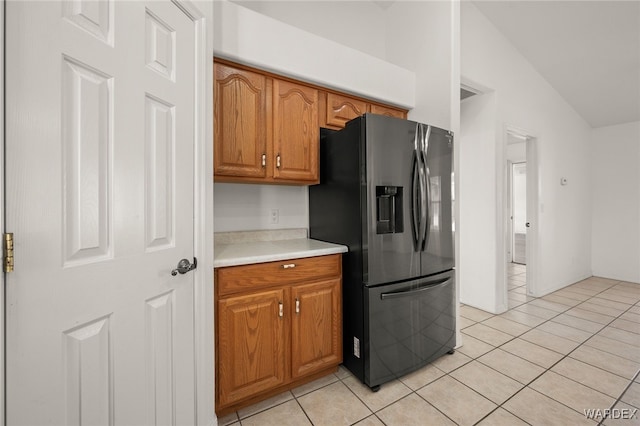 kitchen with light tile patterned floors, lofted ceiling, light countertops, stainless steel refrigerator with ice dispenser, and brown cabinets