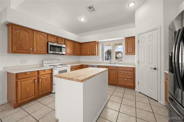 kitchen with stainless steel appliances, a sink, a kitchen island, wood counters, and visible vents