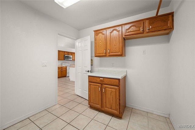 kitchen featuring white range with electric stovetop, brown cabinets, light countertops, stainless steel microwave, and baseboards