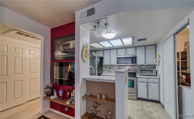 kitchen with appliances with stainless steel finishes, visible vents, backsplash, and gray cabinetry