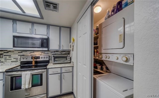 kitchen with visible vents, stacked washer / dryer, appliances with stainless steel finishes, light countertops, and backsplash