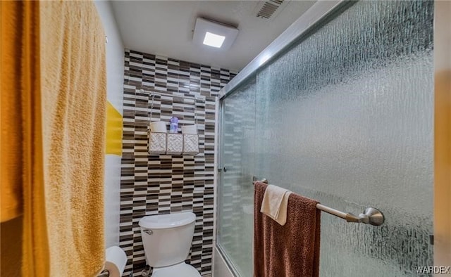 bathroom with visible vents, combined bath / shower with glass door, tile walls, and toilet