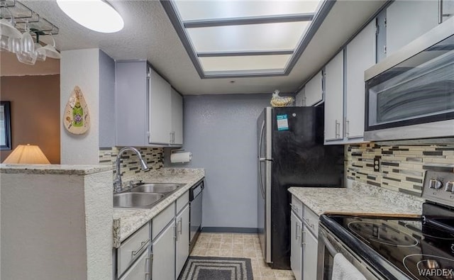 kitchen featuring stainless steel appliances, tasteful backsplash, light countertops, a sink, and baseboards