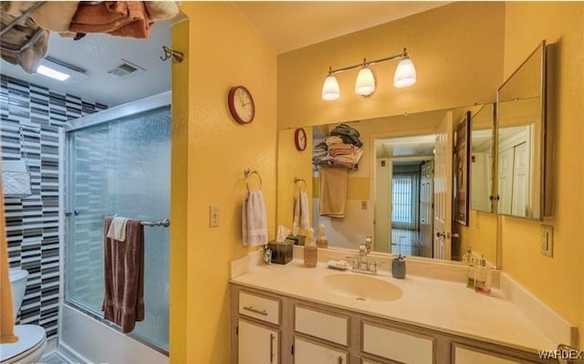 bathroom with toilet, visible vents, bath / shower combo with glass door, and vanity