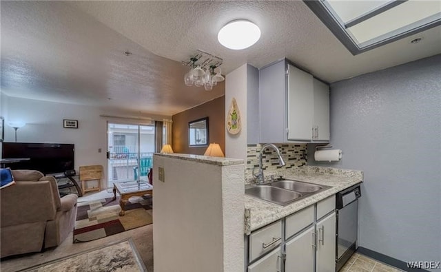 kitchen with light countertops, decorative backsplash, open floor plan, a sink, and a peninsula