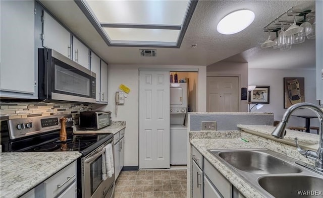 kitchen featuring stacked washer / dryer, a sink, visible vents, light countertops, and appliances with stainless steel finishes