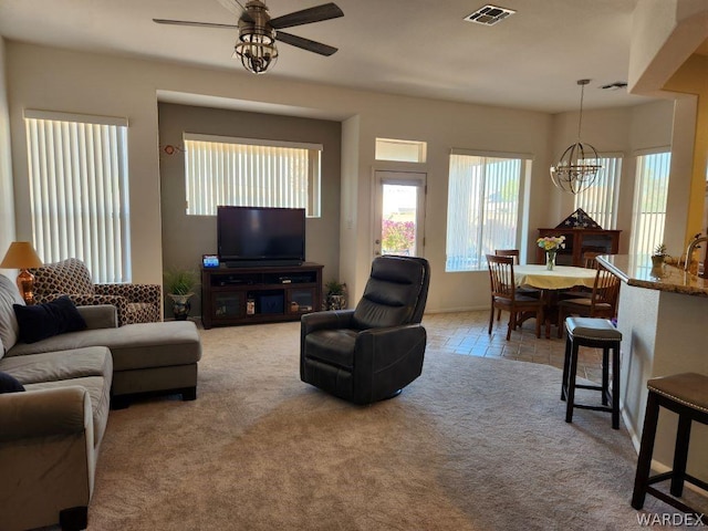 living area with ceiling fan with notable chandelier, visible vents, and light colored carpet