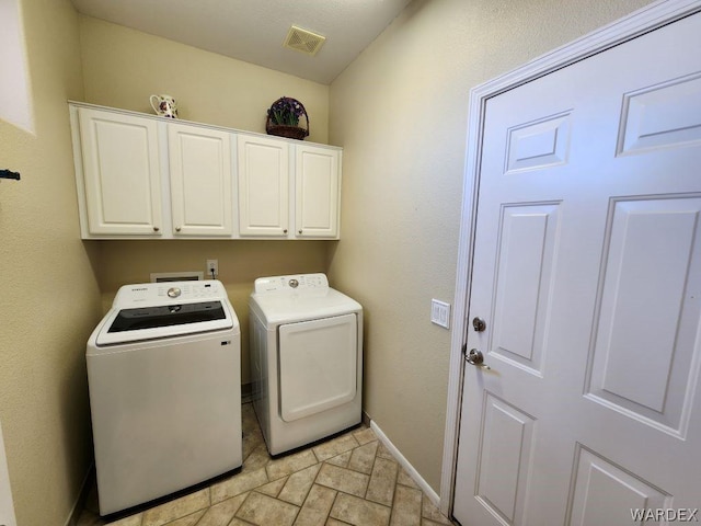 washroom featuring washer and clothes dryer, visible vents, cabinet space, stone finish floor, and baseboards