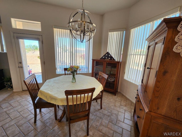 dining space with baseboards, a healthy amount of sunlight, stone tile flooring, and an inviting chandelier