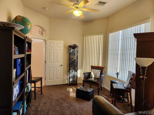 living area with ceiling fan, dark colored carpet, and visible vents