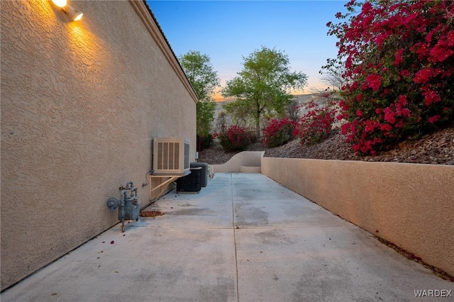 property exterior at dusk featuring cooling unit, a patio area, and stucco siding