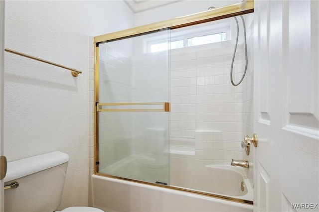 bathroom with a textured wall, shower / bath combination with glass door, and toilet