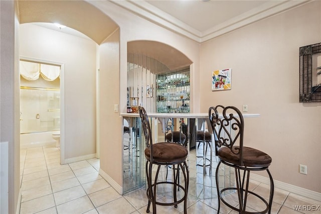 bar featuring arched walkways, baseboards, light tile patterned flooring, and a dry bar