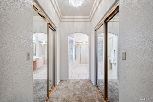 hall with light carpet, arched walkways, and a textured wall