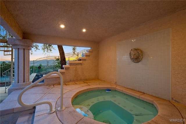 pool at dusk featuring a gate and an indoor in ground hot tub