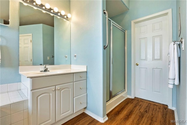 full bath with baseboards, a shower stall, vanity, and wood finished floors