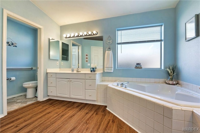 bathroom with a garden tub, toilet, wood finished floors, vanity, and baseboards