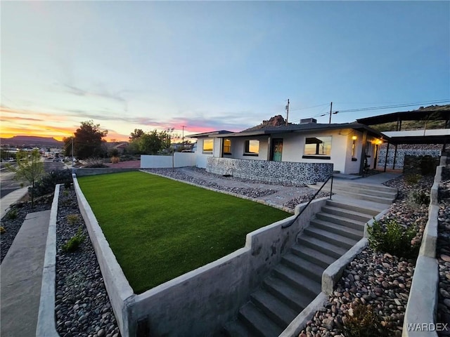 back of house at dusk with a yard and stucco siding