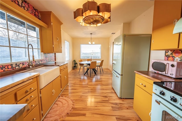 kitchen with light wood-style flooring, a notable chandelier, white appliances, a sink, and decorative light fixtures