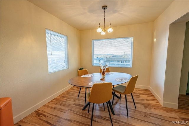 dining room with light wood-style floors, a notable chandelier, and baseboards