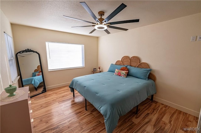 bedroom featuring a ceiling fan, light wood-type flooring, a textured ceiling, and baseboards