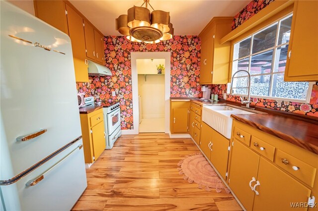 kitchen featuring under cabinet range hood, white appliances, dark countertops, and wallpapered walls