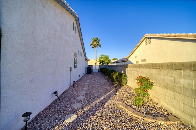 view of side of home with a fenced backyard, a tiled roof, and stucco siding