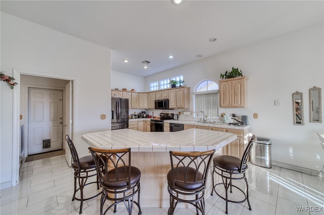 kitchen featuring light brown cabinets, a sink, a kitchen bar, recessed lighting, and black appliances