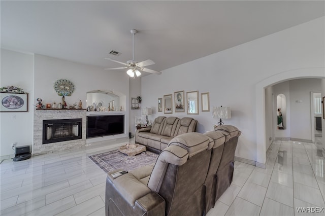 living area with ceiling fan, a fireplace, arched walkways, visible vents, and baseboards
