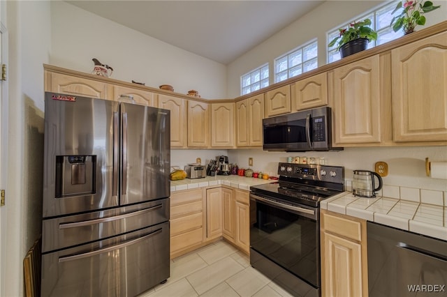 kitchen featuring appliances with stainless steel finishes, light tile patterned floors, light brown cabinetry, and tile counters