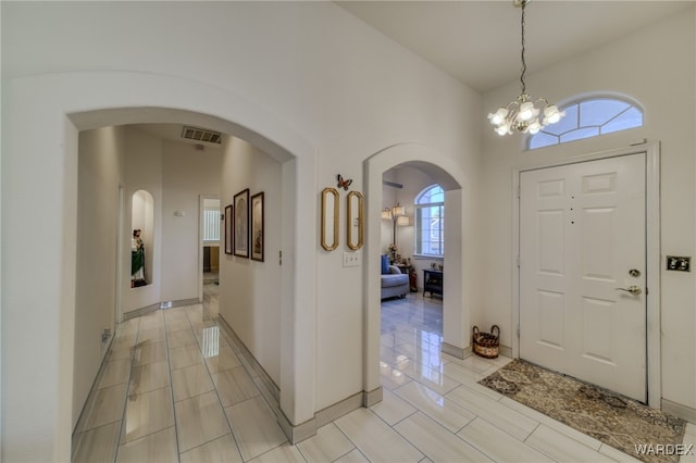 entryway with a chandelier, arched walkways, light tile patterned floors, and visible vents
