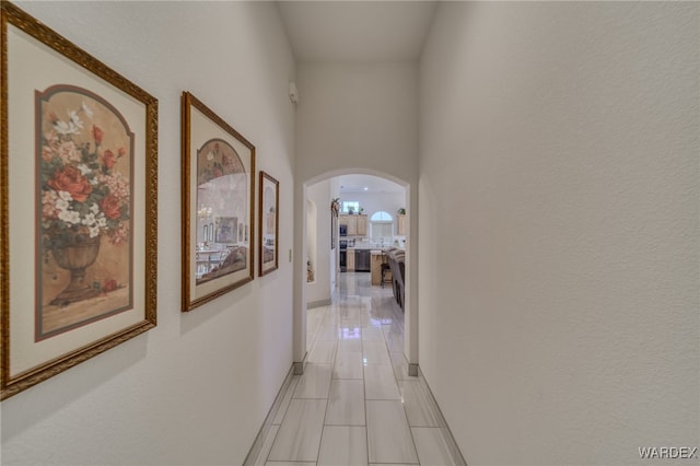hall featuring arched walkways, a high ceiling, and light tile patterned flooring