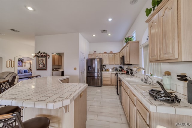 kitchen featuring stainless steel appliances, washer and dryer, tile countertops, and light brown cabinetry