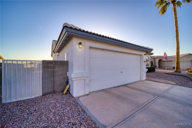 garage at dusk featuring concrete driveway and fence